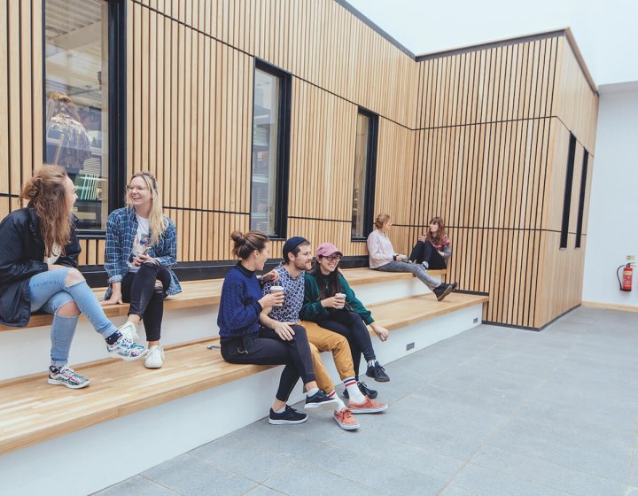 Falmouth University students sitting on steps with a wooden cladded wall behind