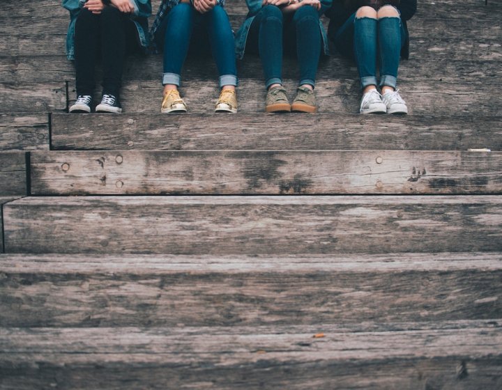 Four people sitting on steps wearing jeans and trainers