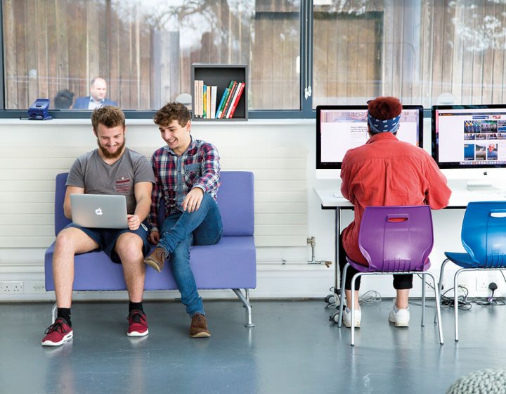 Three business management students working at a laptop and desktop