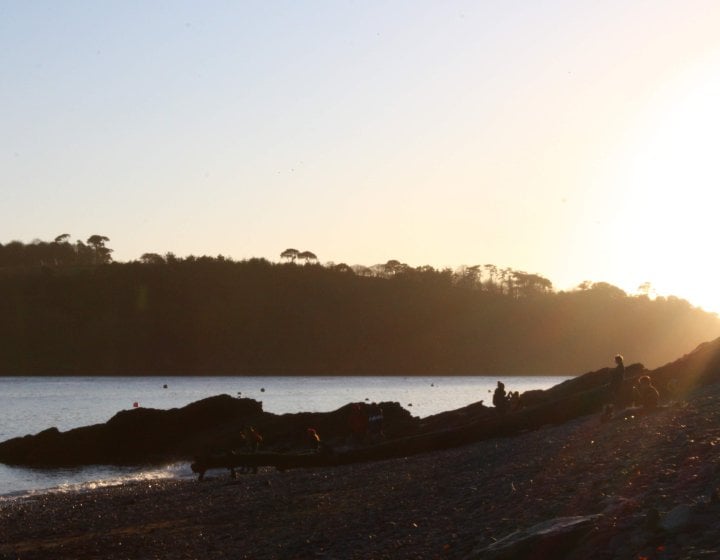 Durgan beach with the sun setting behind trees