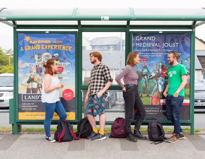 Students stood at bus stop leaning and chatting.