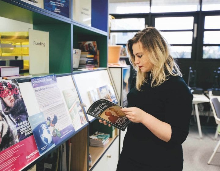 A Falmouth University student looking through a Postgraduate study guide