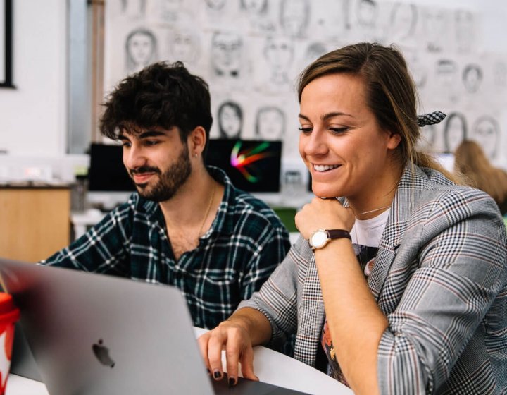 Two Falmouth University Creative Advertising students smiling at a laptop