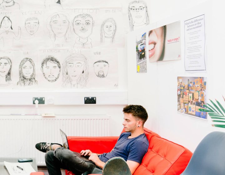 Male Creative Advertising student sitting on a red sofa at Falmouth University