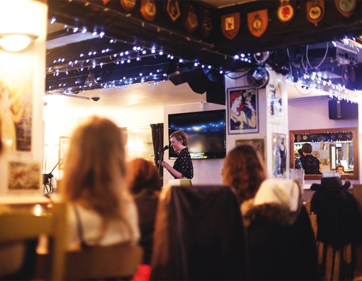 Student speaking into microphone at event in pub surrounded by blue fairy lights.