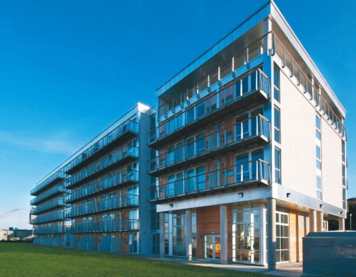 five-storey apartment building with glass balconies, grass and blue sky
