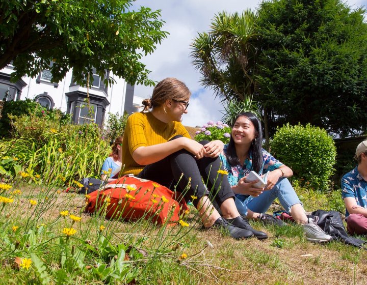 Falmouth University students sat and chatting in gardens on Falmouth Campus