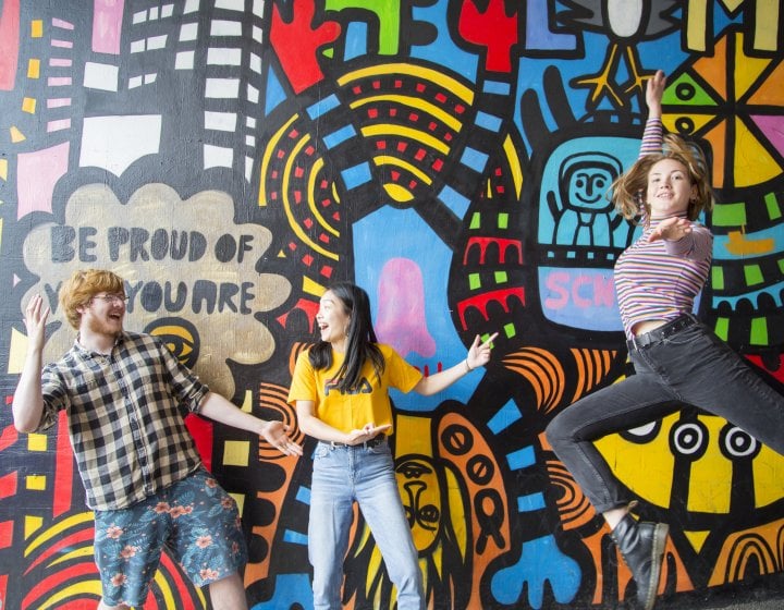 Students jumping in front of brightly coloured mural.
