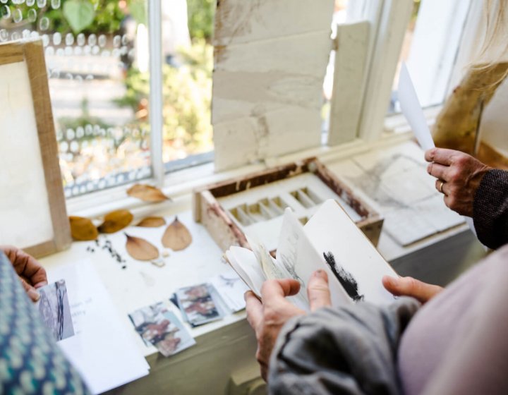 A close up of hands looking through sketchbooks and artworks on a table