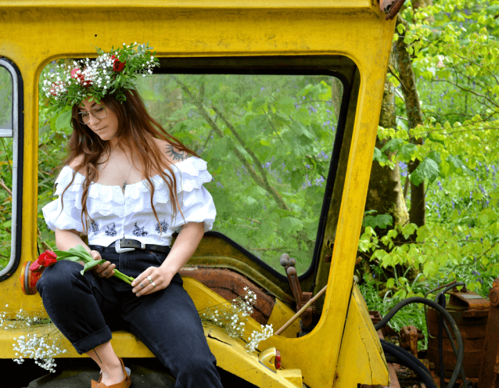 A woman wearing a flower crown sitting on a yellow machine in the woods
