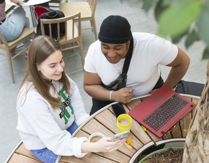 Two students sitting at a table with a laptop and drinks