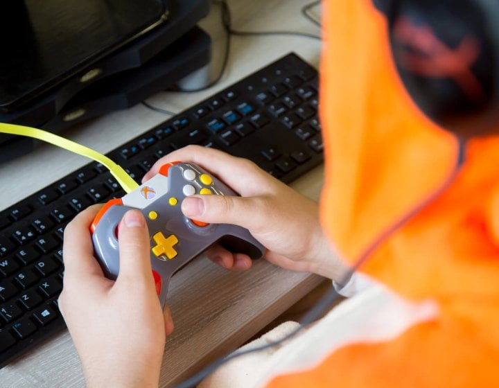 Hands holding a gaming controller in front of a computer keyboard