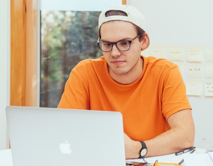 Student in orange t-shirt working on a MacBook.