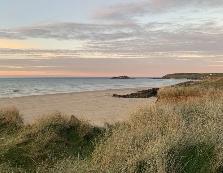 Godrevy beach with grass in the foreground and the sun setting in the background