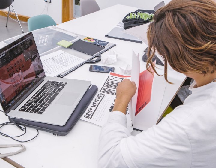 Graphic Design student at a laptop with papers