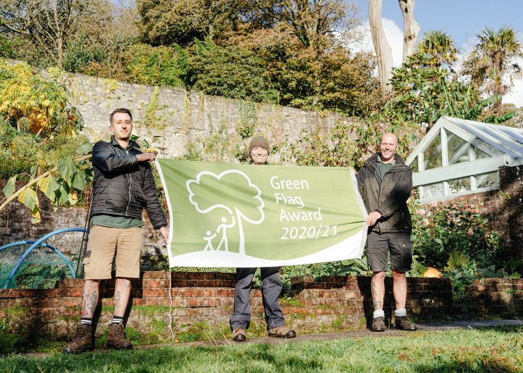 Three people holding up a banner in gardens