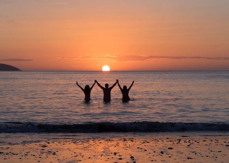 Three Falmouth University students in the sea as the sun is setting