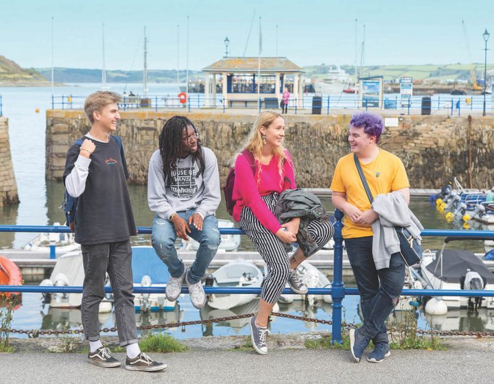 Falmouth University students sitting by the harbour on a sunny day