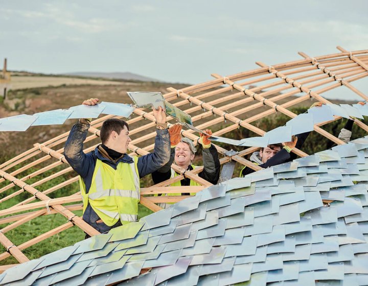 Students adding a roof to a wooden curved structure.