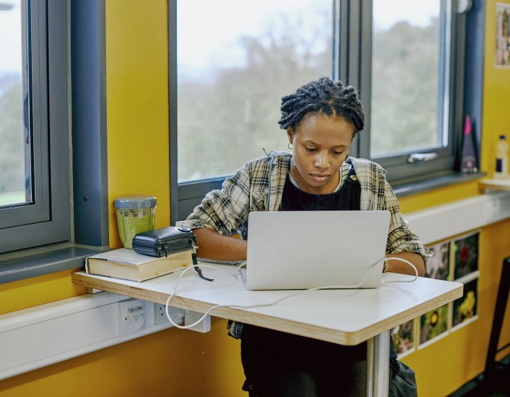 A student sat at a table with a laptop and yellow walls