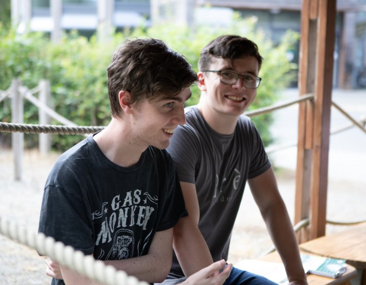 Two male students seated outside and smiling