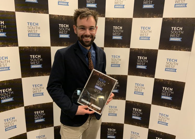 Lecturer holding the Tech South West Award, with a backdrop with branding on it.