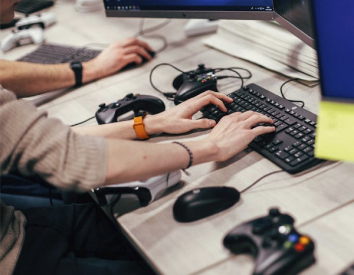 Hands typing on a keyboard with playstation controllers on the table