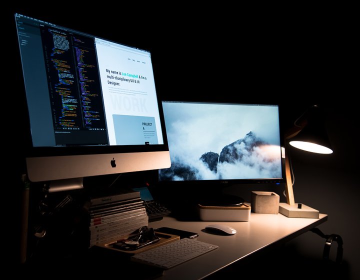 Desktop screens lit up in a dark room.