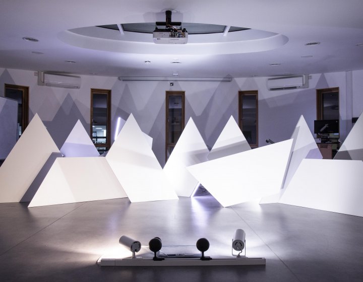 White triangle sculptures in a room lit with purple light