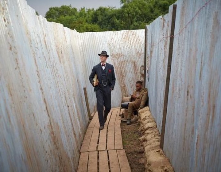 Person in a suit and hat walking through a trench with soldier