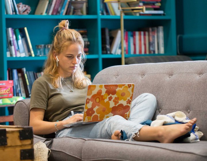 A student reclines on a sofa, working on her laptop