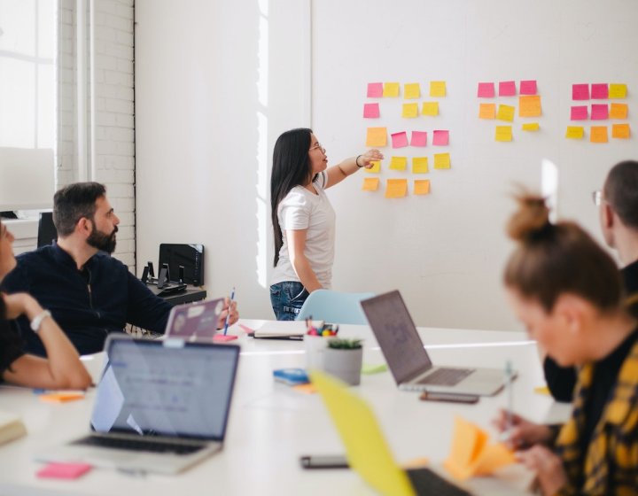 People sat around a table and woman standing with post-it notes on the wall