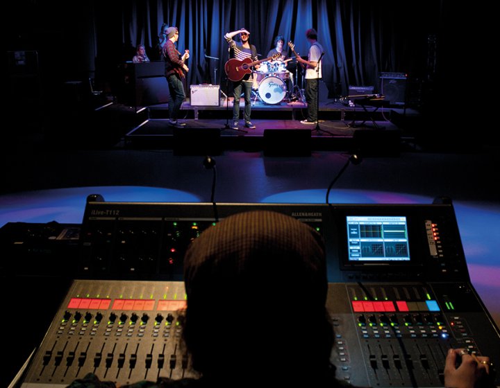 A person at a music desk while a band is on stage performing