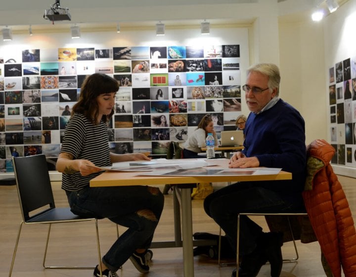 A student and lecturer sat at a table with a photo montage on the wall