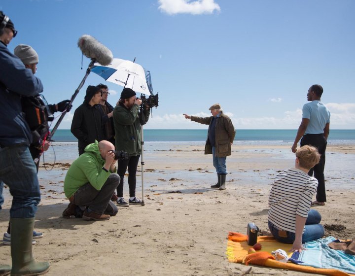 Film and TV students from Falmouth University filming a scene on a beach with blue sky