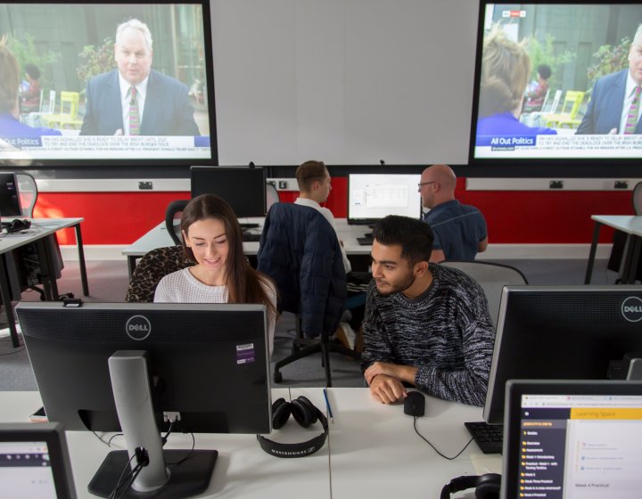 Students working together in newsroom, news playing on screens behind them.