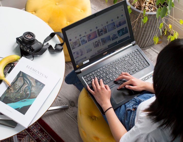 A student working on a laptop next to a white table with a camera and magazine