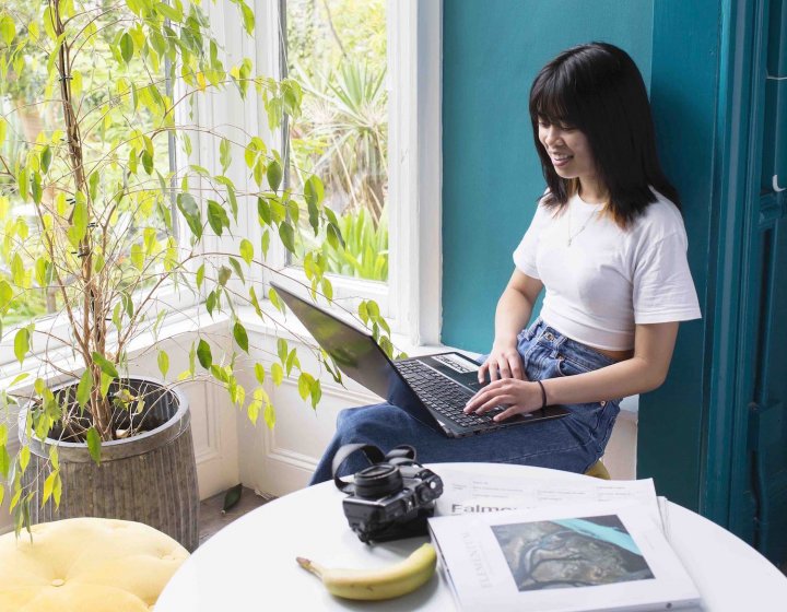 A Falmouth University student on a laptop next to a large indoor plant
