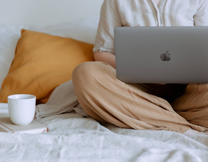 A person sat crossed legs with an apple mac and a cup