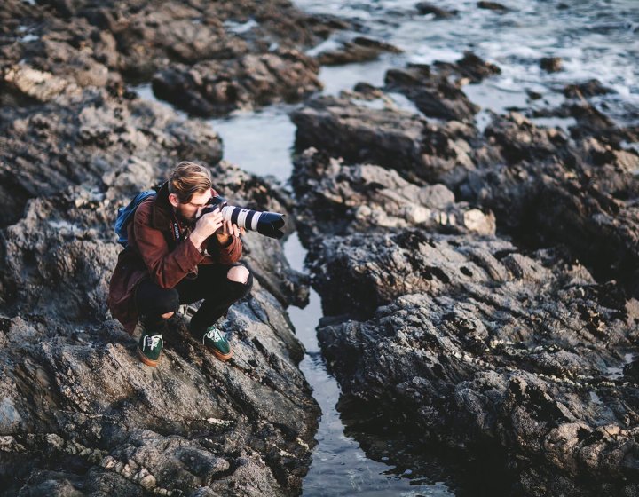 Falmouth University Photography student sits on rocks photographing the sea