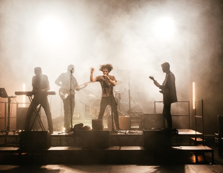 Shadowy figures of a four piece band playing on a smokey stage.