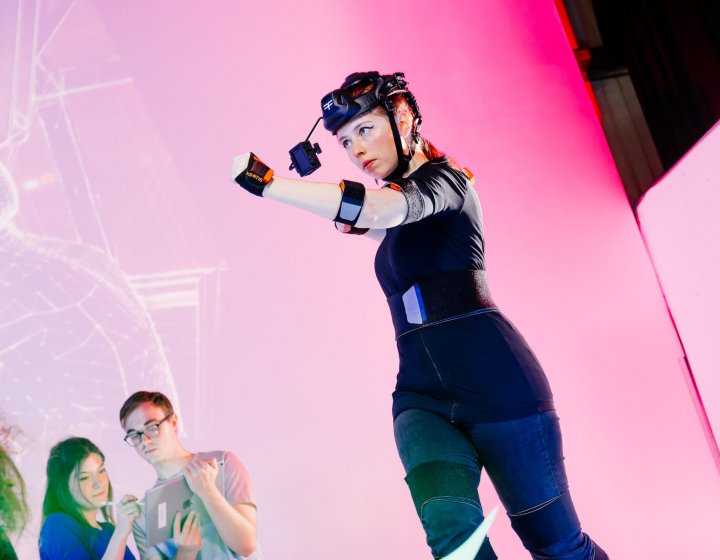 Female student wearing games development headset in front of a pink background