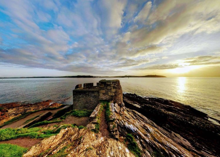 Ruins of a castle on a cliff with the sea and sun in the background