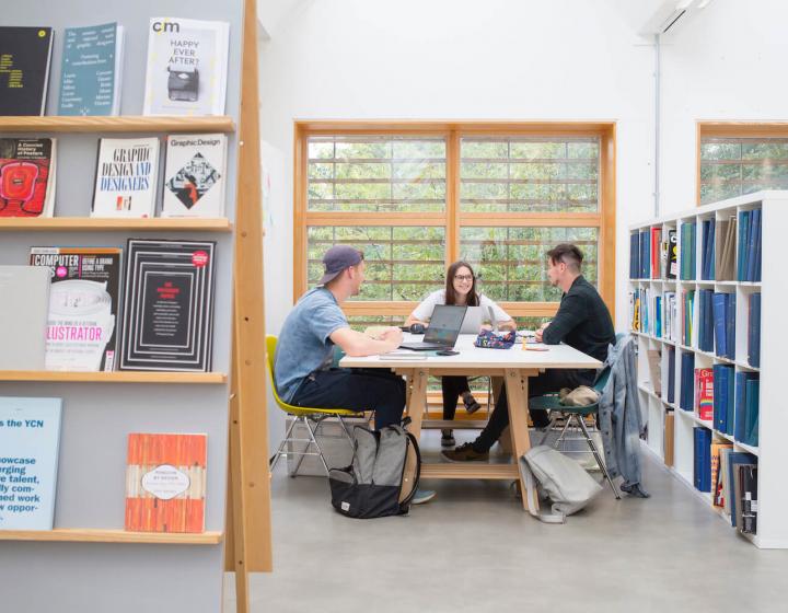 Three students sat at a table in a Graphic Design studio at Falmouth University