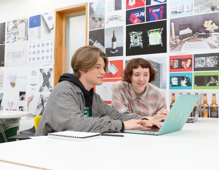 Two Falmouth University students working together at a laptop in a graphic design studio