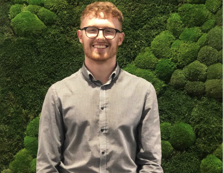 Will Dorrell Business and Entrepreneurship graduate standing in front of green moss wall.