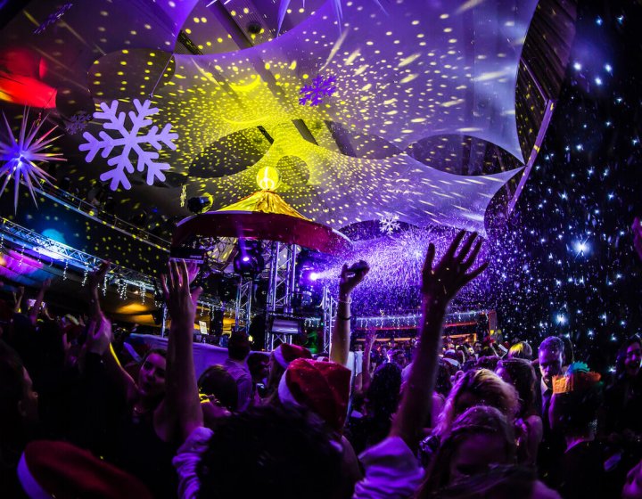 Dark room with disco lights and students dancing with arms in the air.
