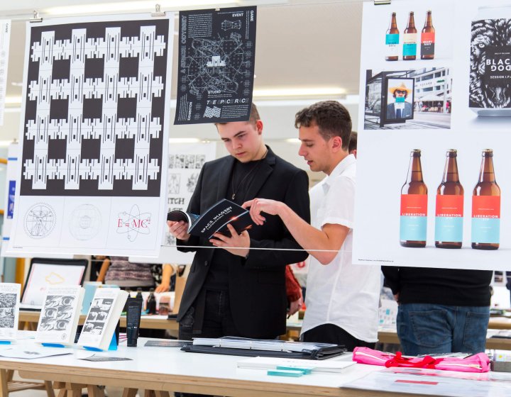 Students looking through a book, design work hanging from a line in front of them.
