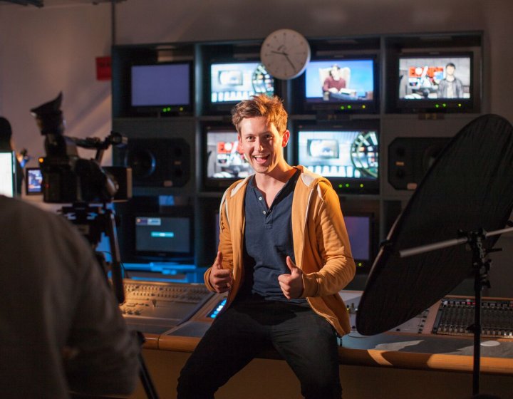 Student giving the thumbs up in television control studio.