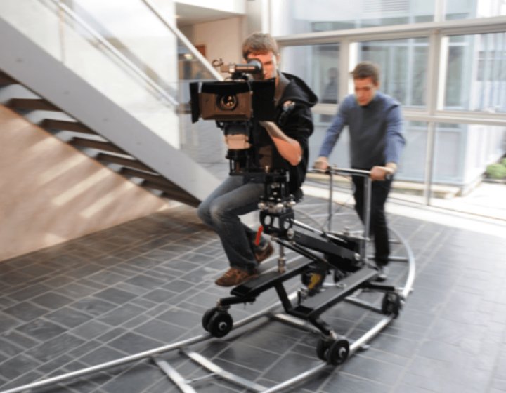 Student behind camera on camera dolly being moved along a track.